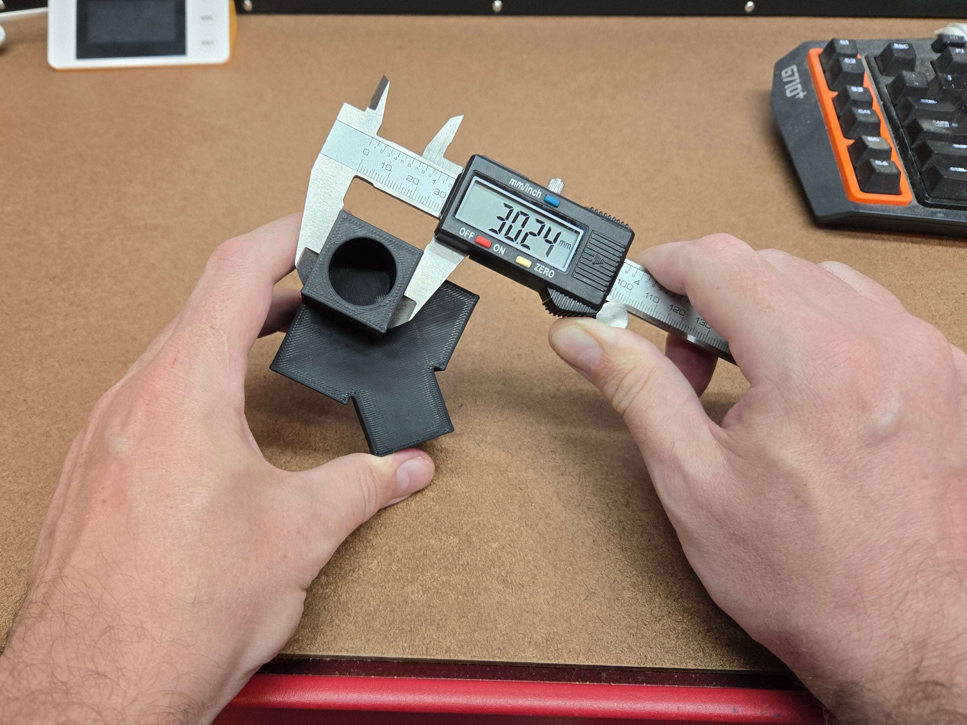 Person using a digital caliper to measure a black object on a wooden workbench.